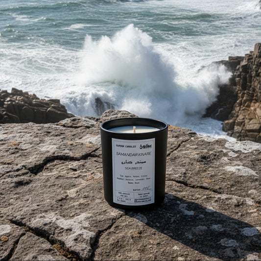 Black candle with a white label on a rocky surface against an ocean vista with crashing waves