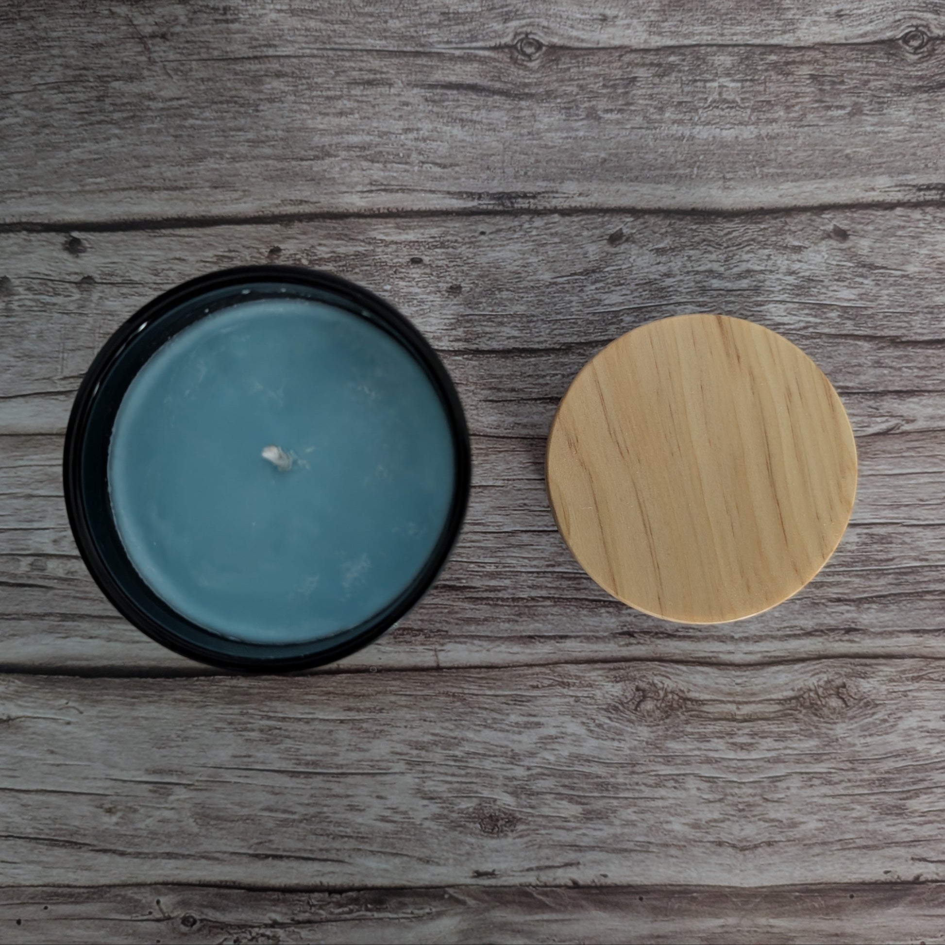 Blue candle in a black container with a wooden lid on a wooden surface